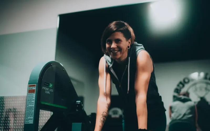 Active woman smiling during workout in gym setting with leg curl machine.