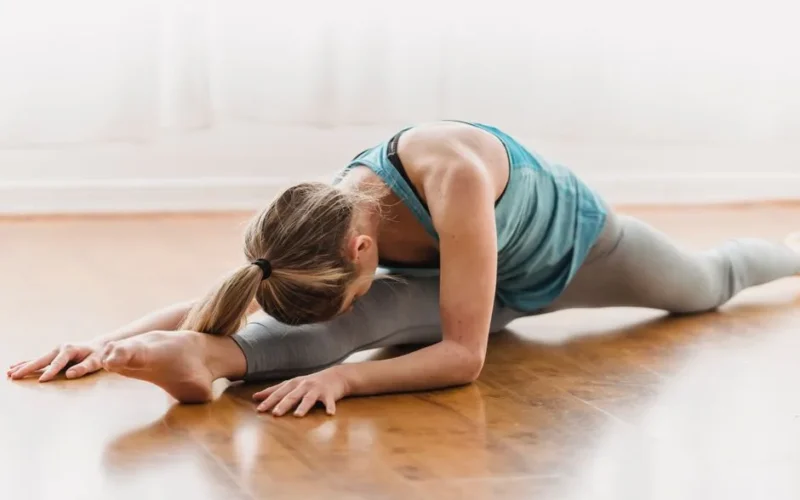 Slim active anonymous female in sportswear stretching on timber floor of home in daylight