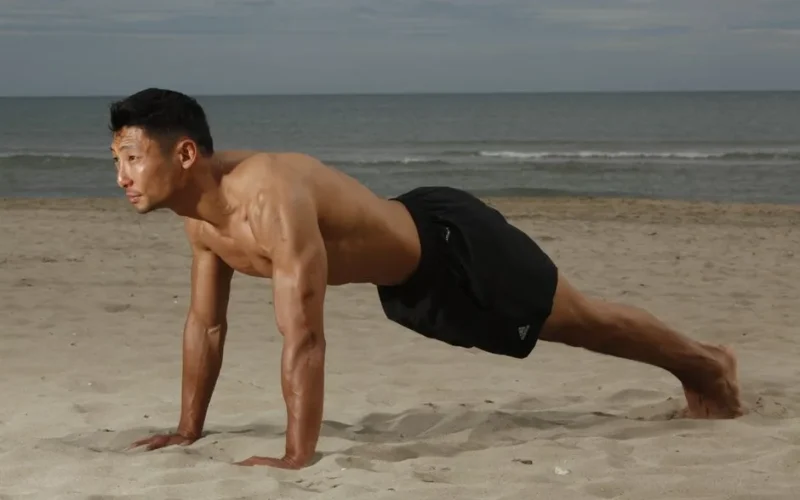 Fit man doing a plank exercise on a sunny beach, showcasing strength and fitness.