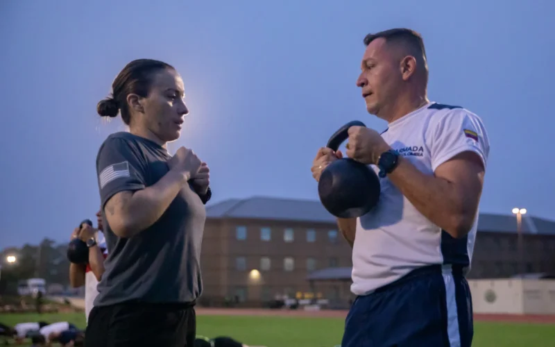 U.S. Army Sgt. 1st Class Jeannine Valencia, instructor at the Holistic Health and Fitness Academy, Leader Training Brigade, shows Colombian army Sgt. Maj. Danny Salazar Arias, student at the Colombian Armed Forces Sergeants Major Academy, proper technique for a kettlebell squat during a physical training session with Programa Integral para Suboficiales de Alta Jerarquía (PISAJ) 21 students and facilitators at Fort Jackson, S.C. Aug. 12, 2025. PISAJ is a biannual, partner nation-funded initiative aligned with U.S. Southern Command’s Theater Campaign Plan and directly supports the Colombian army's transformation to align its noncommissioned officer corps with globally recognized standards. (U.S. Army photo by Staff Sgt. Joshua Taeckens)