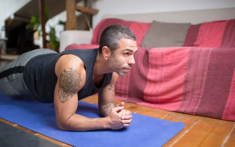 Man doing plank exercise indoors on a yoga mat, embracing a healthy lifestyle.