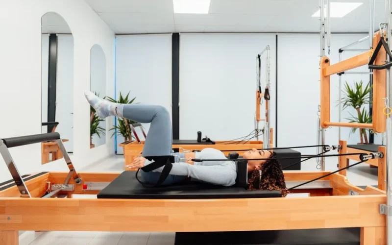 A woman performing fitness exercises on a Pilates reformer in a modern gym setting.