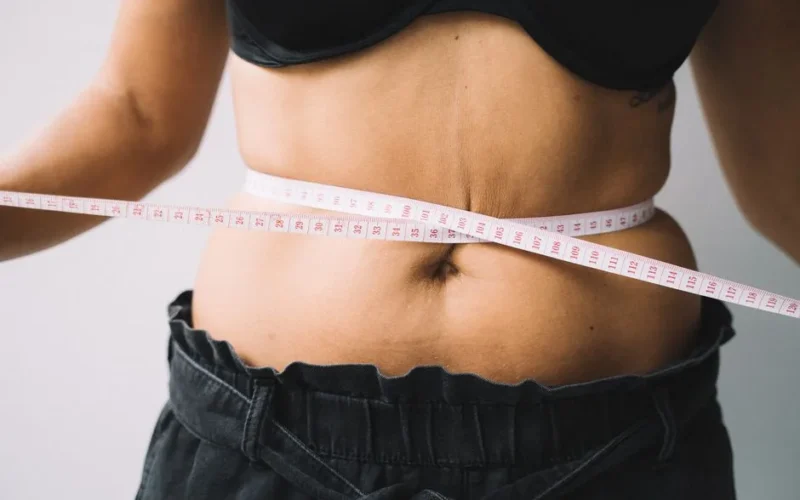 A person measuring their waist with a tape, symbolizing fitness and health goals.