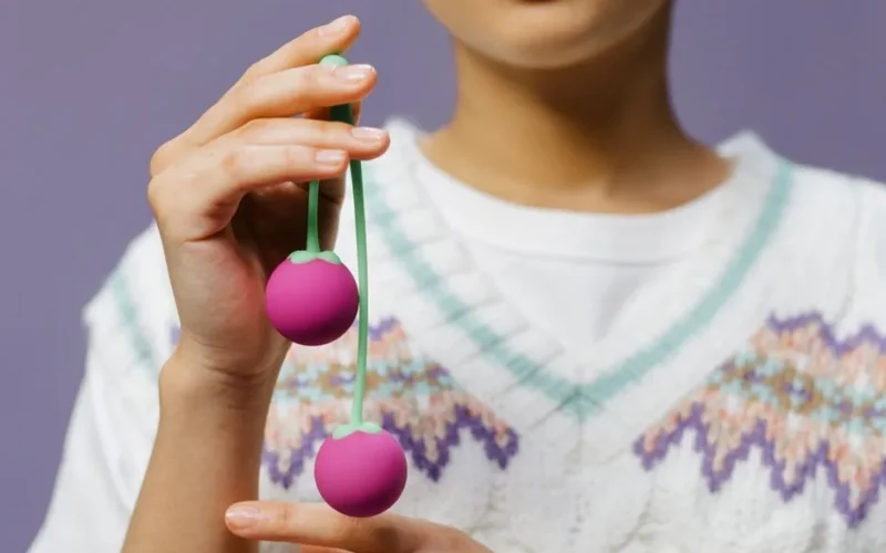 Detailed close-up of hands holding purple Kegel balls against a purple background.