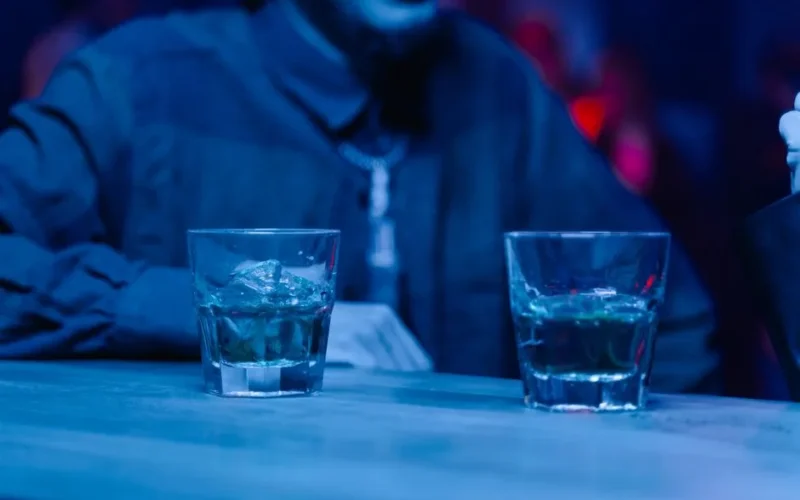 Two glasses of liquor on a bar countertop in a dimly lit nightclub setting.