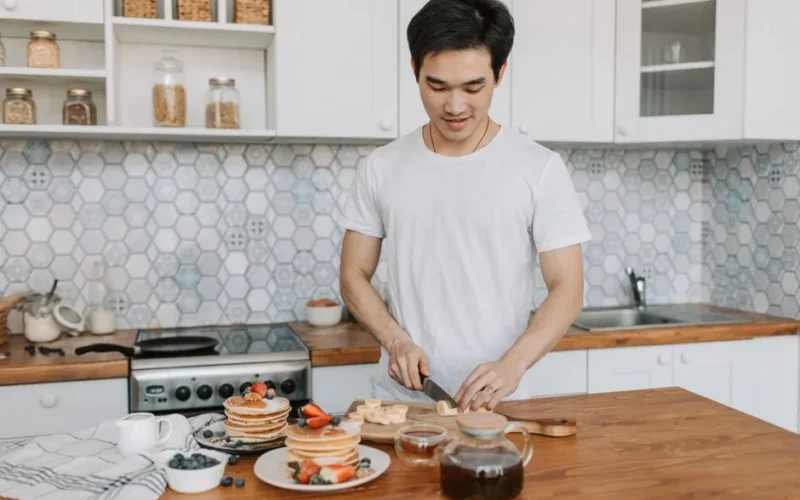 A man slicing bananas for breakfast in a modern home kitchen with fruit pancakes.