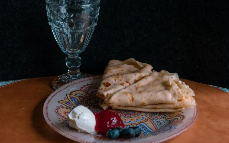 Elegantly set crepes with berries and cream on a patterned plate, showcasing a gourmet presentation.