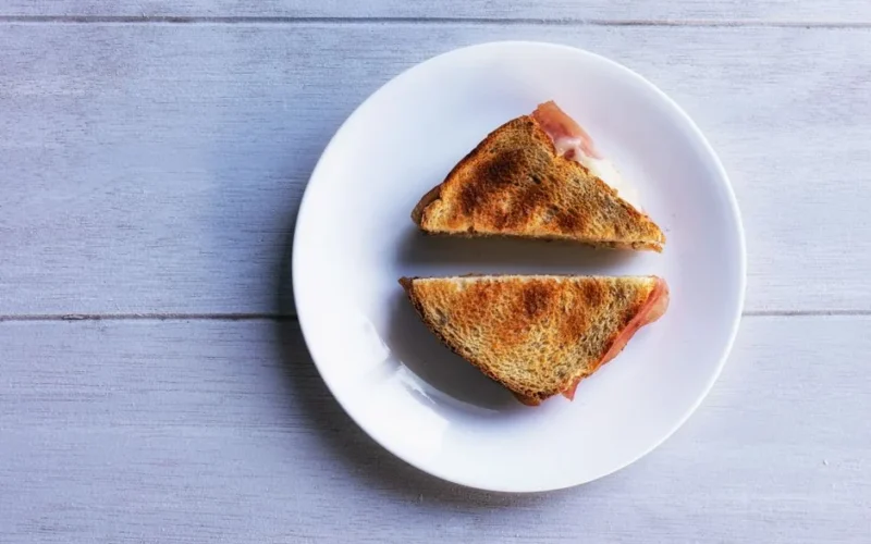 Crispy toasted ham and cheese sandwich served on a white plate, perfect breakfast.