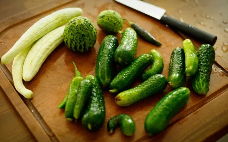 A variety of fresh cucumbers arranged on a wooden chopping board with a knife.