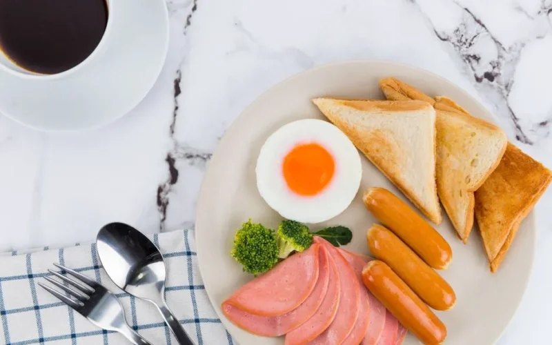 A appetizing breakfast with eggs, sausages, and toast served alongside a cup of coffee.