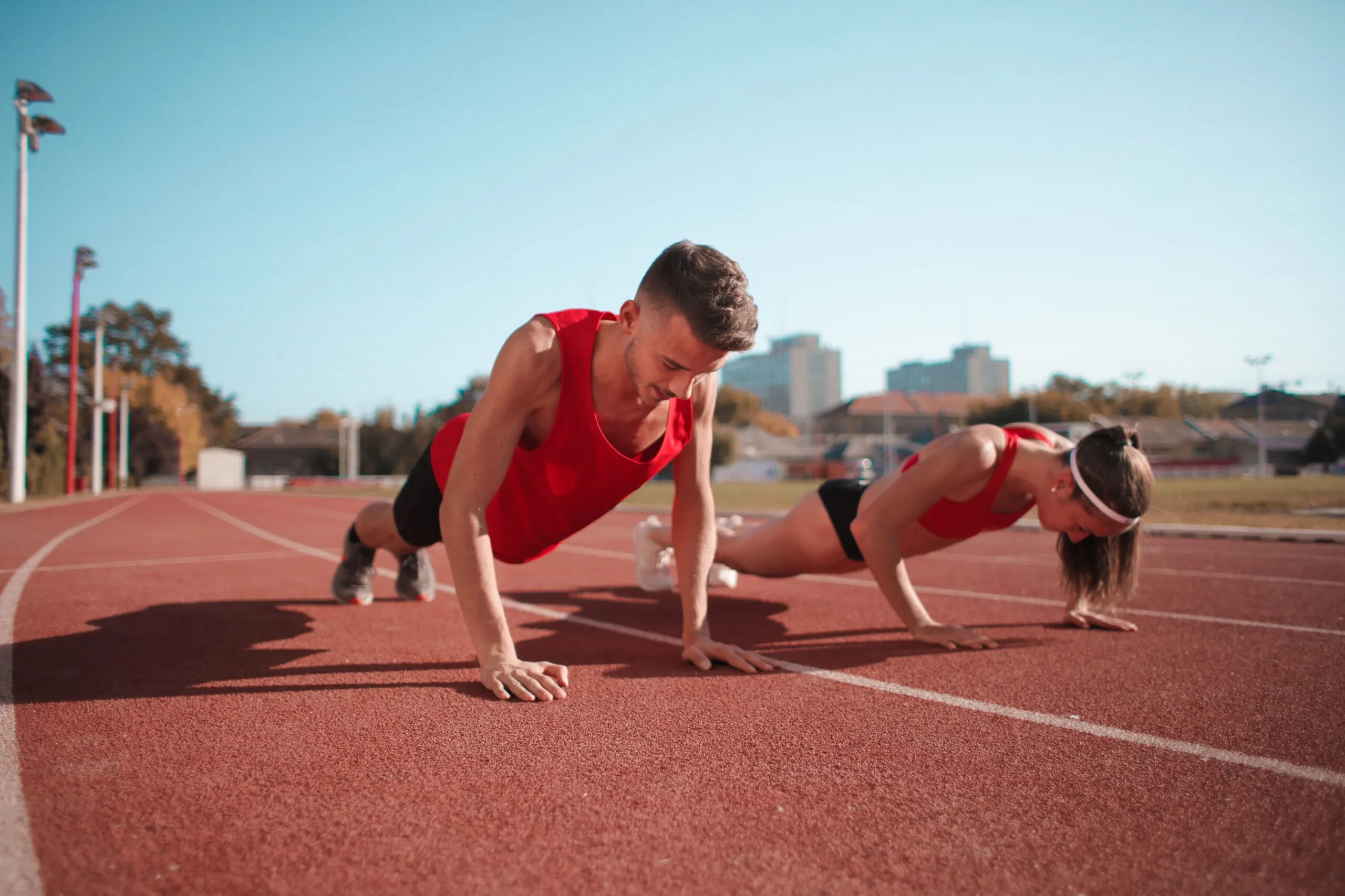 Two athletes doing push-ups on a track during daytime workout session outdoors.