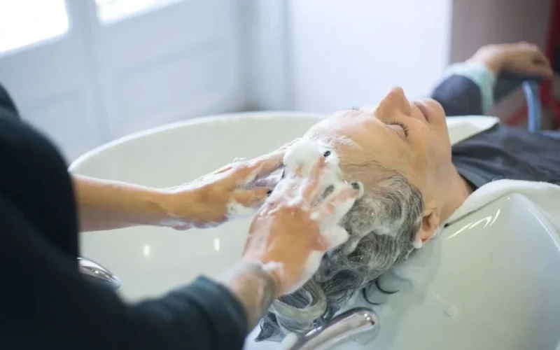 Close-up of senior woman getting hair washed with foam at salon sink, enjoying the pampering session.