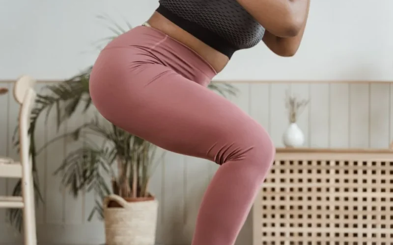 Close-up view of a woman squatting indoors wearing pink leggings and black top.