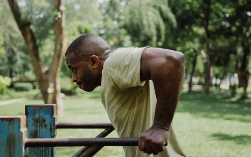 A man exercising by doing dips on parallel bars in a lush outdoor park setting.