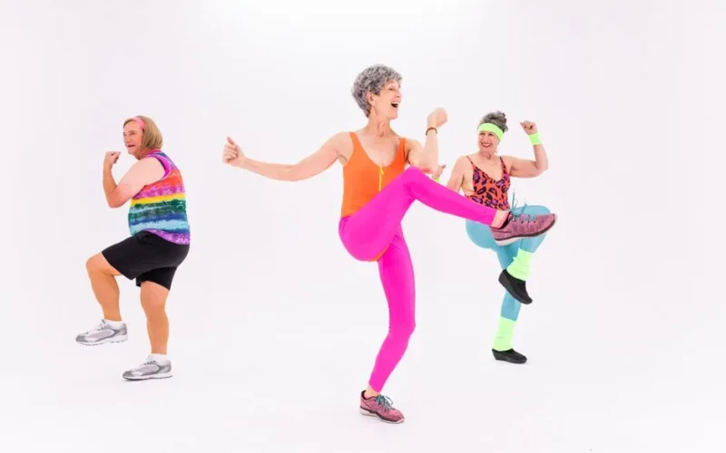 Three senior women having fun and staying fit with energetic aerobics in colorful outfits indoors.