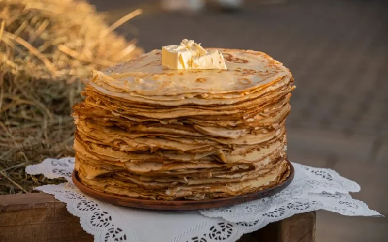A large stack of crepes topped with butter, set against a rustic outdoor backdrop, perfect for food photography.