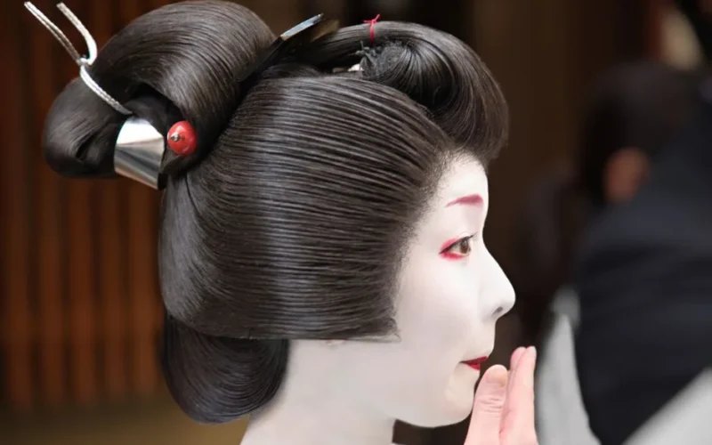 Close-up of a maiko in Kyoto wearing traditional kimono and applying makeup, symbolizing Japanese culture.