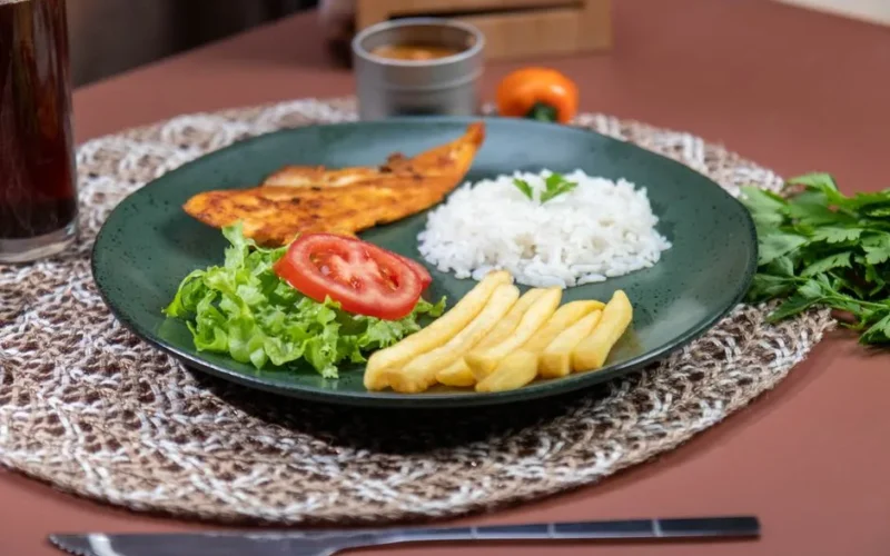 Appetizing meal featuring grilled fish, rice, and fries with fresh salad on a woven mat.