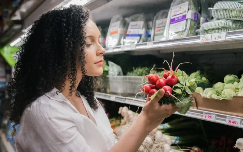Woman in grocery store choosing fresh radishes from the vegetable aisle.