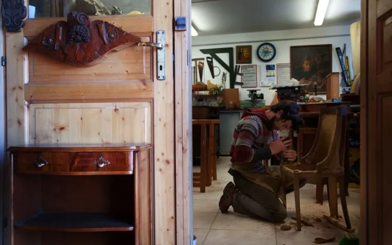 Craftsman skillfully restoring a wooden chair in his workshop. Intricate work surrounded by tools.