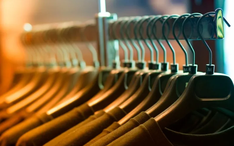 A row of neatly arranged clothes hanging on a rack with wooden hangers.