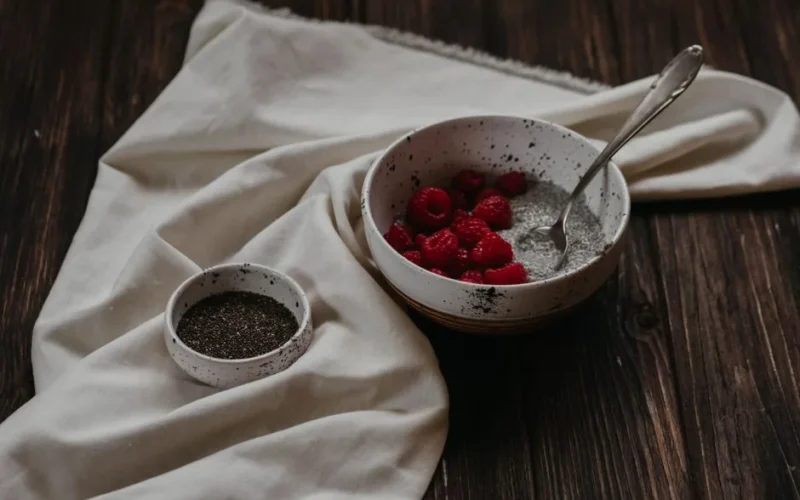 Delicious chia pudding topped with raspberries on a rustic wooden table.