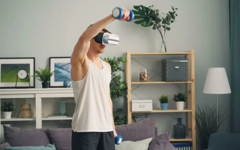 Man exercises using virtual reality headset and dumbbells, indoors.