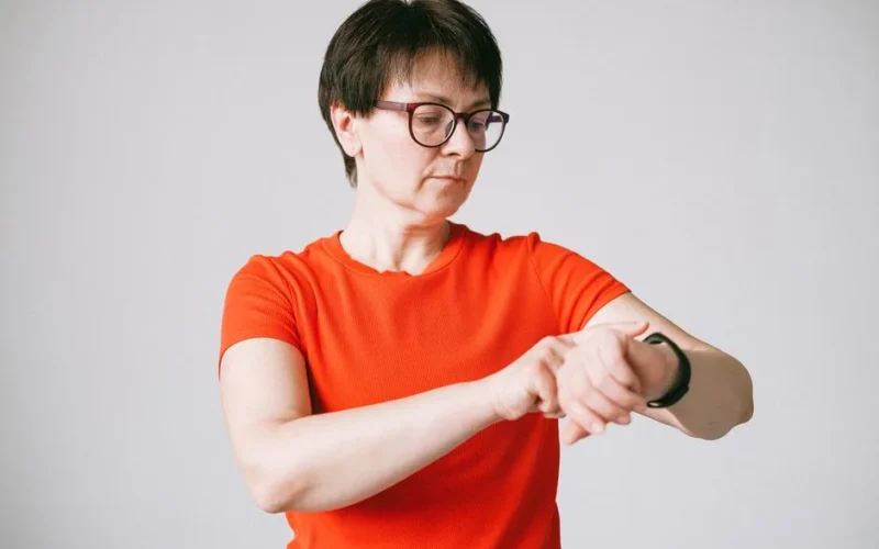 A woman in glasses checks her smartwatch in a minimalist indoor setting.