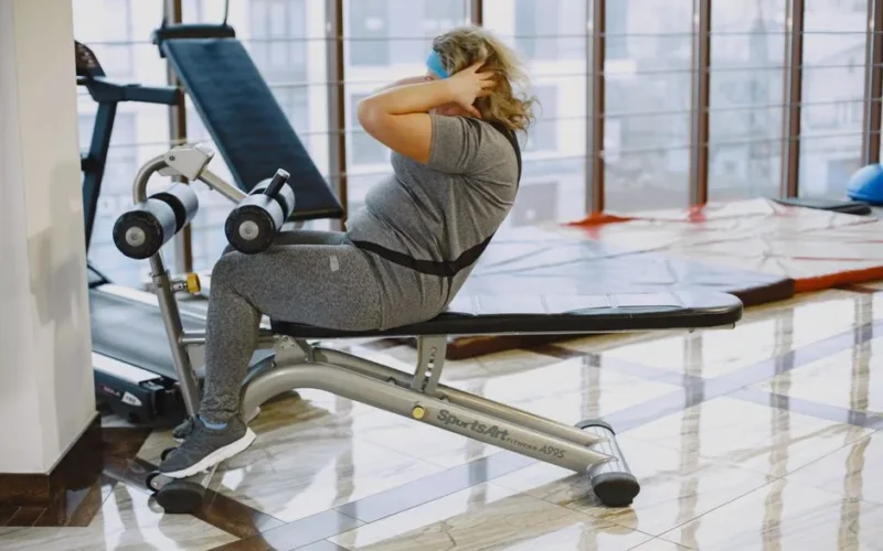 A woman performing sit-ups in a gym using a sit-up bench, focusing on fitness and exercise.