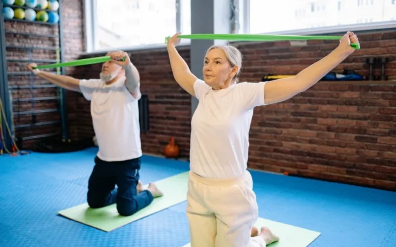Elderly man and woman performing fitness workout with resistance bands, promoting healthy lifestyle indoors.