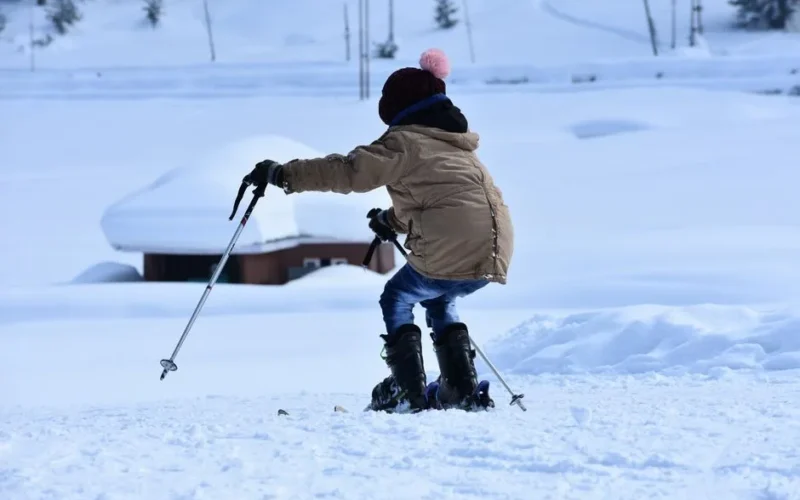 A young child learning to ski on a snowy slope during a bright winter day.