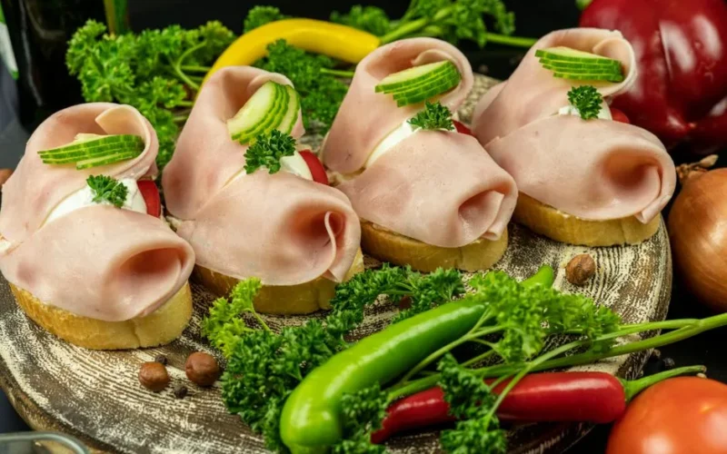 Delicious open-faced sandwiches with ham, cucumber, and parsley on rustic wooden plate.
