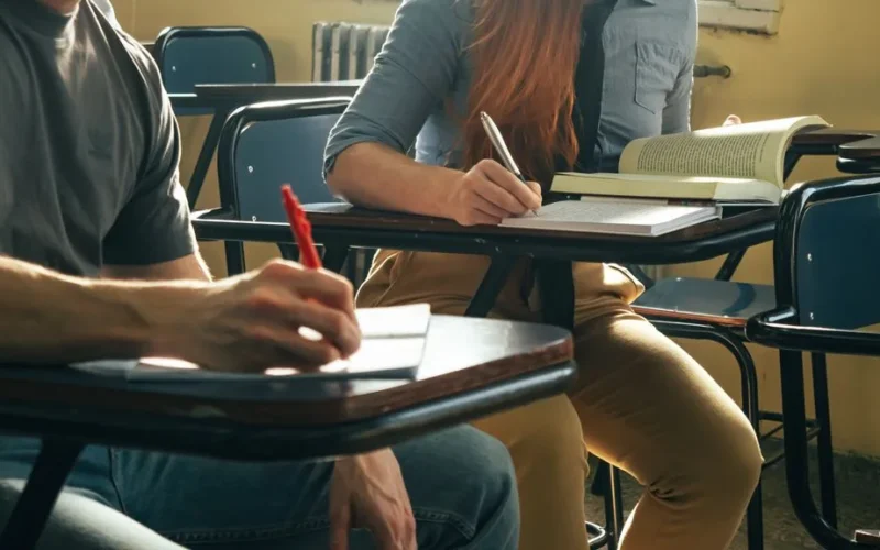 Two students writing notes in a classroom setting, focusing on study and education
