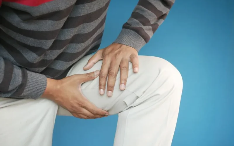 Close-up of a man's hands on his knee, showing pain or injury, on a blue background.