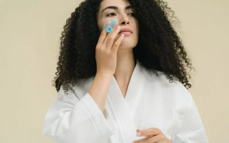 Woman using a facial roller for skincare in a serene indoor environment, promoting self-care and relaxation.