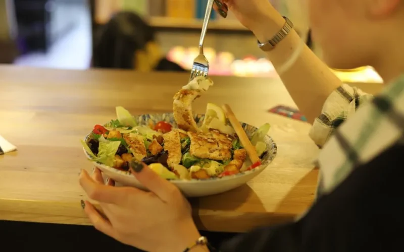 Close-up of a person enjoying a fresh chicken salad at a wooden table indoors.