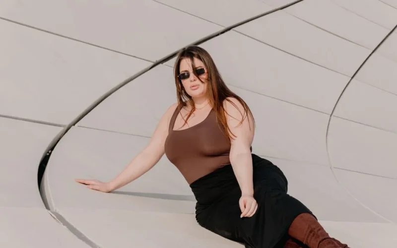 Woman in fashionable attire posing by modern architecture outdoors.