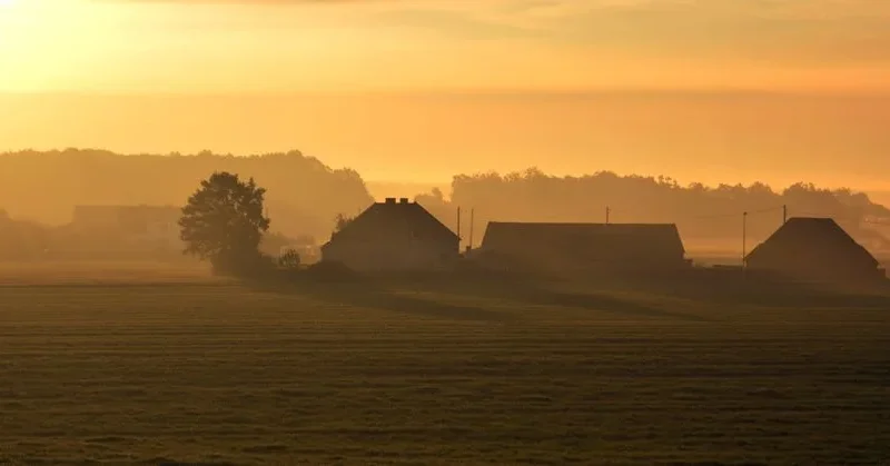 Serene view of a rural landscape in Poland during sunset, with fog and farmhouses.