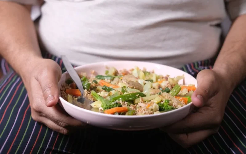 Close-up of an overweight individual holding a nutritious vegetable salad in a pink bowl.
