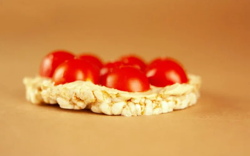A delectable rice cake topped with fresh cherry tomatoes, perfect for healthy snack ideas.