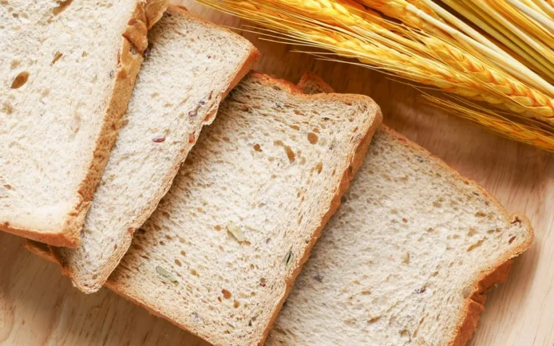 Close-up of sliced whole grain bread on a wooden surface with wheat ears.