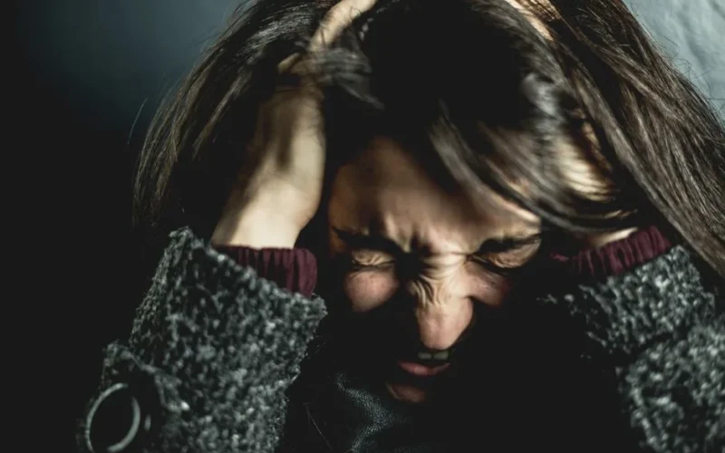Close-up of a woman in distress with eyes closed and hands in hair, expressing anxiety.