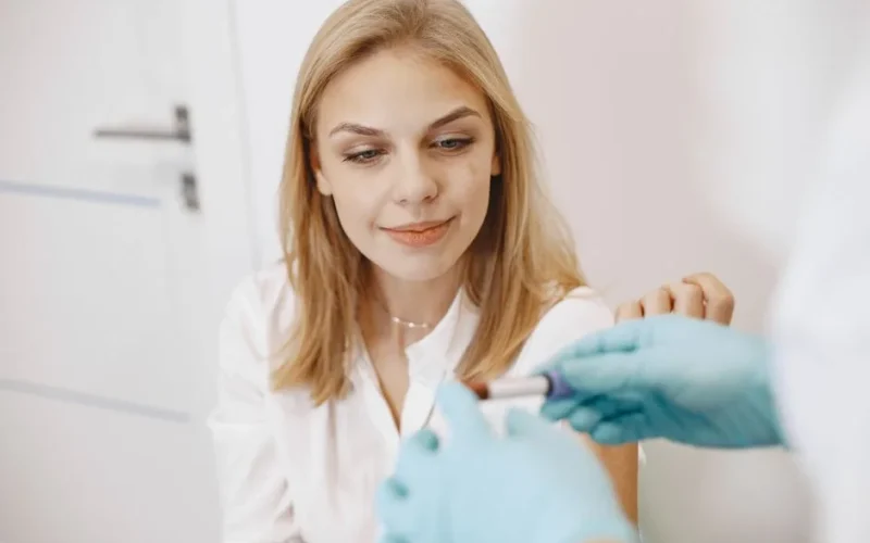 Blond woman in clinic receiving blood test with healthcare professional holding sample.