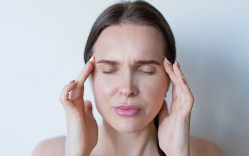 Close-up of a woman with closed eyes holding her temples, showing signs of a migraine or headache.