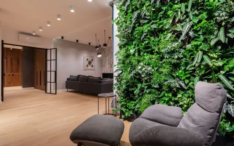 Interior of light modern flat with armchair with pouf near green wall with plants leaves
