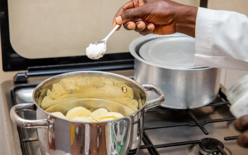 Close-up of a cook adding salt to a pot of boiling potatoes on a stove in Bujumbura, Burundi.