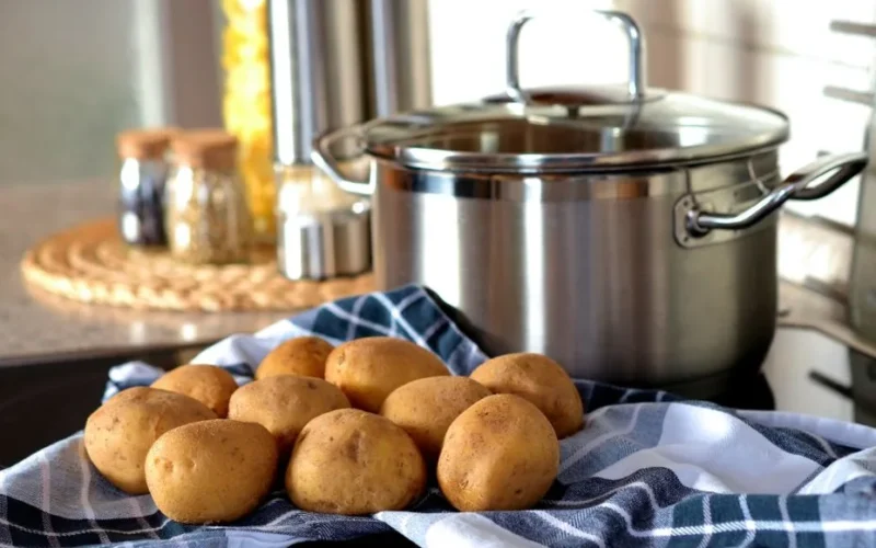 Fresh potatoes on cloth beside a stainless pot, ready for cooking in a modern kitchen.