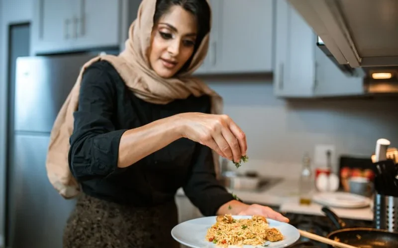 A woman sprinkles herbs on a rice dish, showcasing food preparation skills.