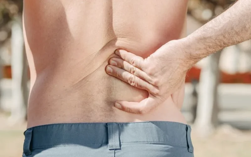 Close-up of a man holding his lower back in pain, possibly indicating discomfort or injury.
