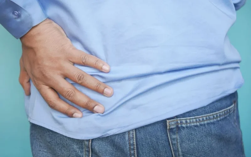 A person in a blue shirt and jeans clutching their hip, possibly indicating pain.